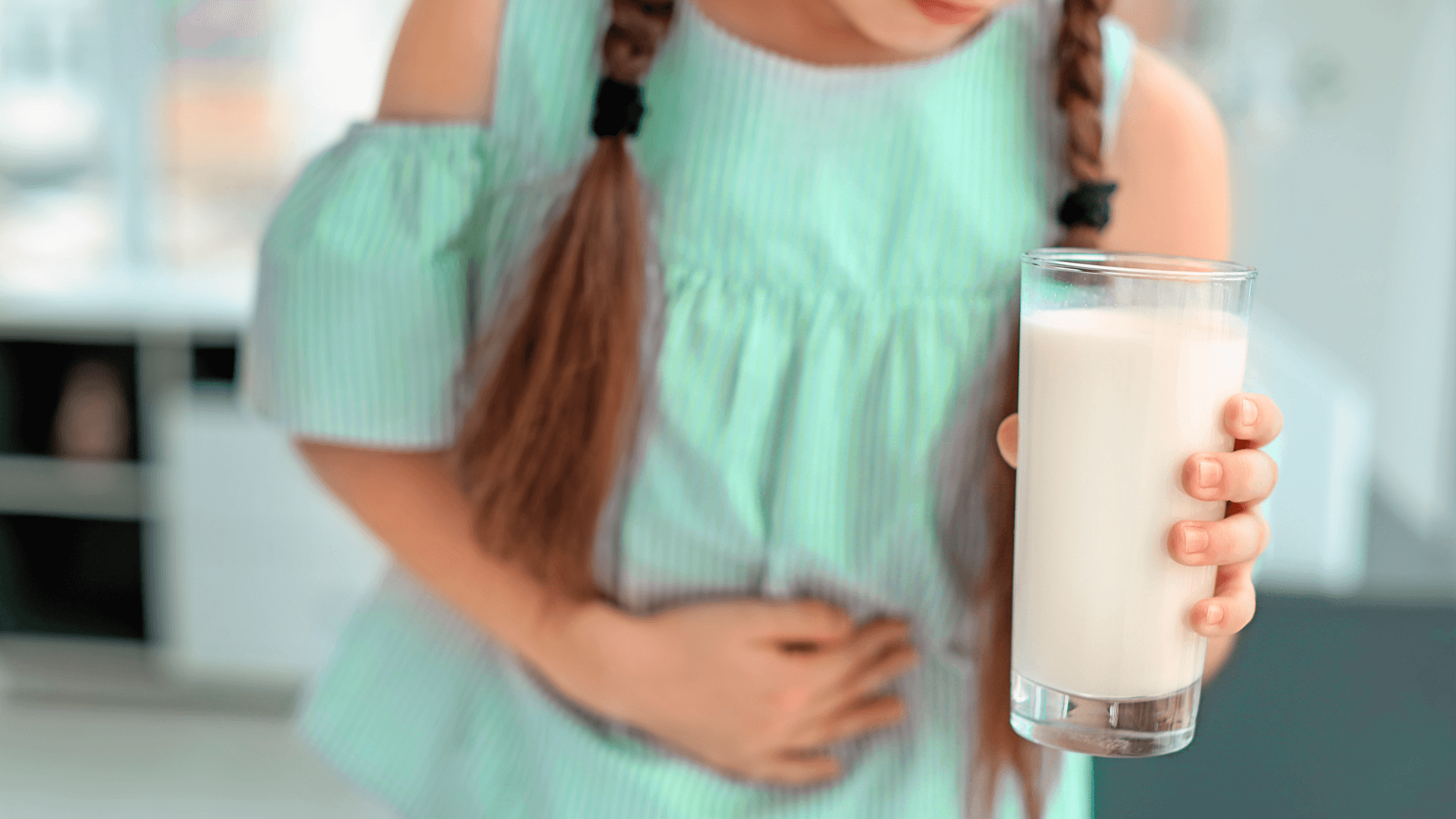 Uma menina com uma mão pressionando a barriga e a outra mão segurando um copo de leite