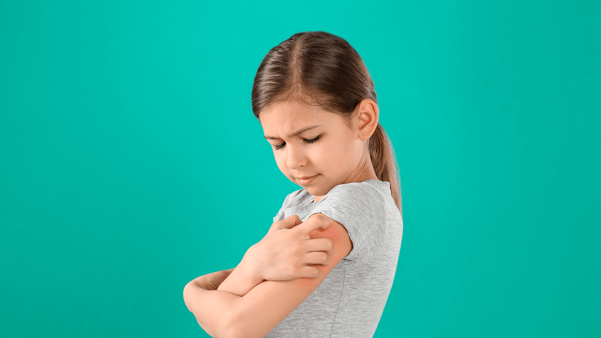 Uma menina na frente de um fundo verde. Seu braço está avermelhado e ela está coçando
