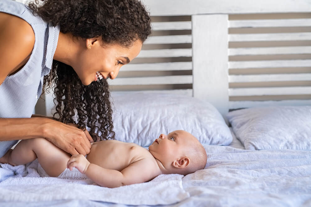Mãe trocando a fralda de bebê antes de saber como coletar urina de bebê