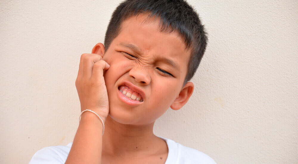 Menino coçando o rosto por causa da Caxumba