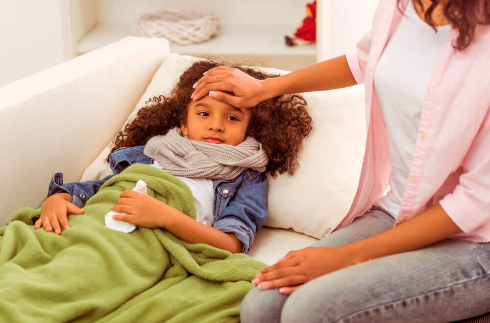 Mãe medindo a temperatura da filha resfriada. A imagem ilustra o post sobre a diferença entre gripe e resfriado.