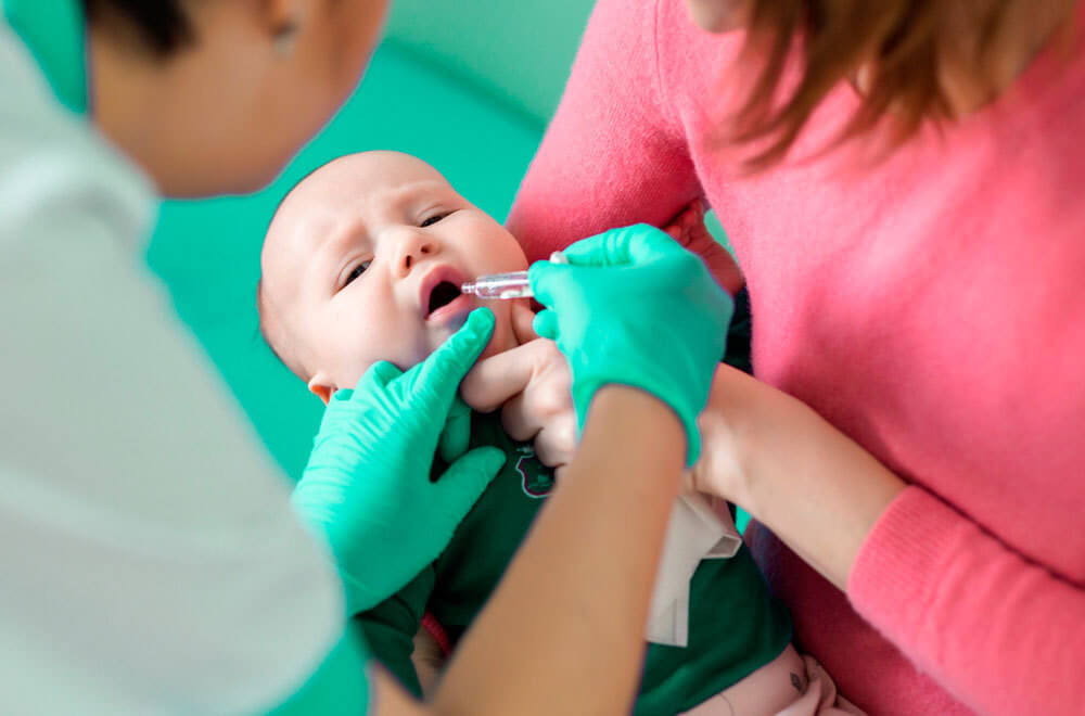Enfermeira aplica a dose da vacina contra o rotavírus de forma oral. A imagem representa o que é rotavírus.