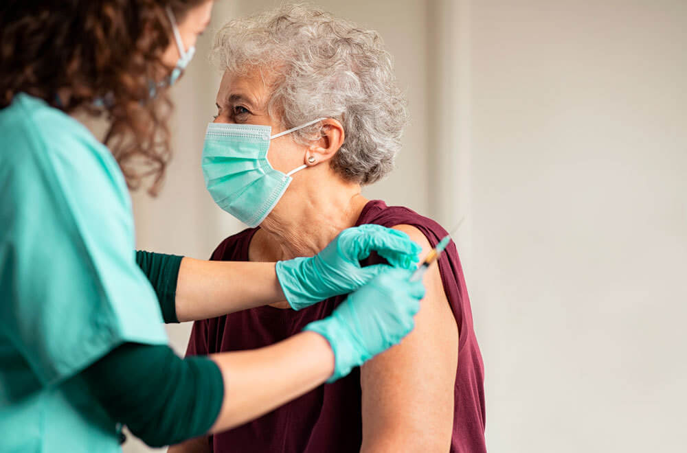 Pessoa idosa de máscara tomando um dos imunizantes recomendados no calendário de vacinação para idosos
